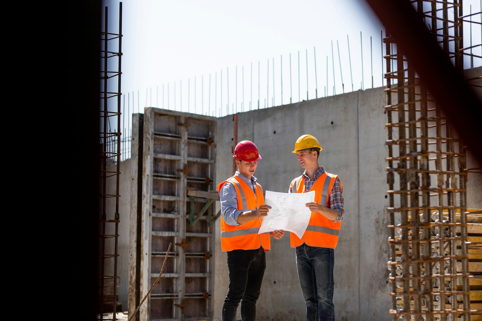 Civil engineer and construction manager in orange work vests and hard helmets explore construction